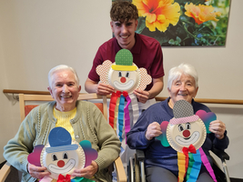 Drei Personen halten große Clowns-Figuren aus Papier in einem freundlichen Raum.