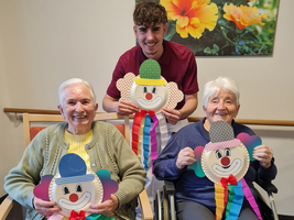 Drei Personen halten große Clowns-Figuren aus Papier in einem freundlichen Raum.