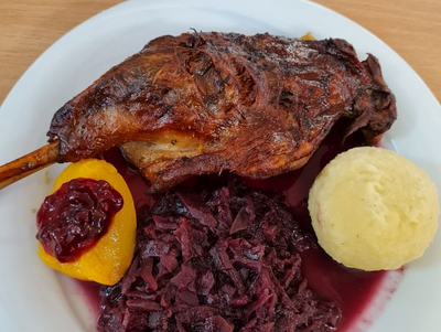 Bratente mit Rotkohl, Knödel und einer Scheibe Pfirsich auf einem Teller.