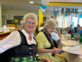 Zwei Frauen in traditioneller Kleidung lächeln bei einer Feier an einem Tisch.