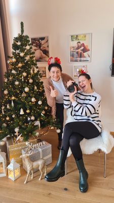 Zwei Frauen mit Kamera und Weihnachtsbaum, lächelnd in festlicher Stimmung.