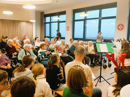Eine Gruppe von Menschen sitzt bei einer Aufführung in einem Gemeinschaftsraum.
