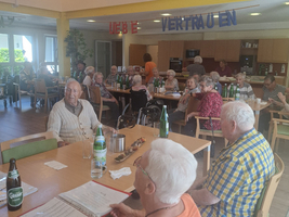 Eine Gruppe älterer Menschen sitzt gemeinsam beim Essen in einem hellen Raum.