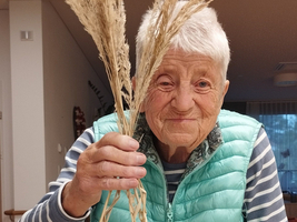 Eine ältere Frau hält einen Weidenkorb mit dekorativen Halmen.