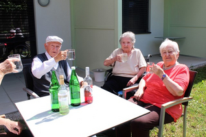 Drei ältere Menschen stoßen mit Gläsern auf einer Terrasse an.