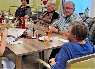 Fünf ältere Menschen sitzen an einem Tisch und genießen Getränke und Snacks.