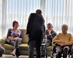 Eine Gruppe älterer Menschen sitzt auf einem Sofa in einem hellen Raum.