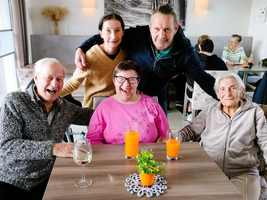 Fünf Personen lächeln an einem Tisch mit Getränken in einem gemütlichen Café.