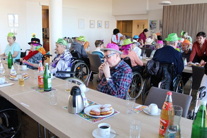 Ältere Menschen in bunten Hüten feiern gemeinsam in einem Speisesaal.