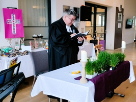 Ein Pfarrer hält eine Andacht an einem dekorierten Tisch mit Kerzen und Gras.