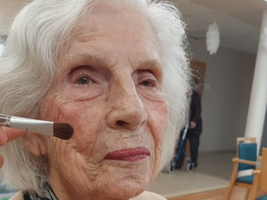 Eine ältere Frau bekommt Make-up aufgetragen, während sie freundlich schaut.