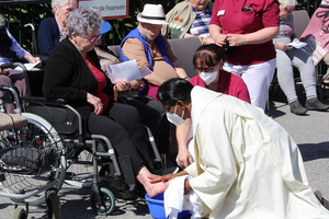 Ein Priester wäscht die Füße einer älteren Dame im Freien.