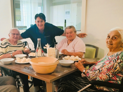 Betreuerin und Seniorinnen genießen gemeinsam ein Essen bei einem Tisch.