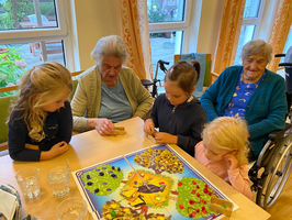 Ein Stammtisch mit älteren Frauen und jungen Mädchen, die gemeinsam ein Spiel spielen.