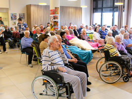 Eine Gruppe älterer Menschen sitzt in einem Gemeinschaftsraum auf Stühlen und Rollstühlen.