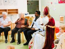 Sankt Nikolaus sitzt mit mehreren Personen in einem Raum für eine Feier.