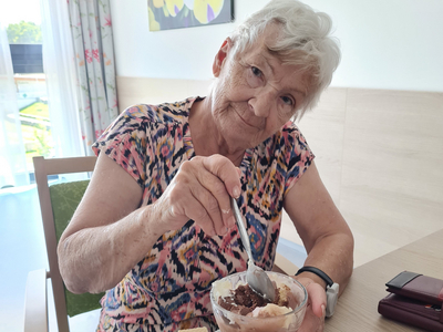 Ältere Frau genießt ein Dessert mit Eis und Waffel an einem Tisch.