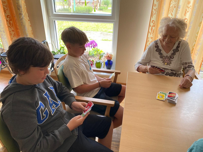 Drei Personen spielen gemeinsam Karten an einem Tisch in einem hellen Raum.