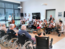 Musikveranstaltung mit Akkordeonspielern und Zuschauern in einem Gemeinschaftsraum.