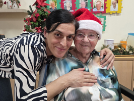Eine Frau umarmt einen älteren Herrn mit Weihnachtsmütze lächelnd.