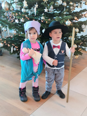 Zwei Kinder in Kostümen vor einem geschmückten Weihnachtsbaum.