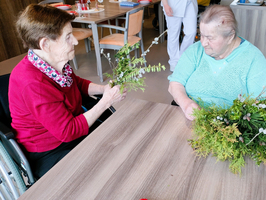 Ältere Frauen sitzen um einen Tisch mit Pflanzenmaterial für Bastelarbeiten.