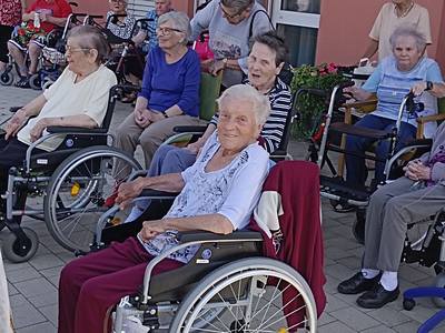 Gruppierung älterer Menschen in Rollstühlen, lächelnd im Freien.