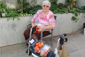 Eine ältere Frau sitzt mit Obst auf ihrem Rollator in einem Garten.