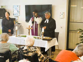 Zwei Geistliche halten eine Feier in einem Festsaal vor Senioren ab.