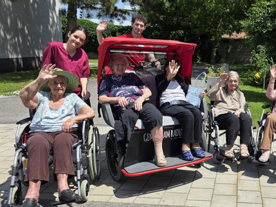 Gruppe älterer Menschen und Pflegekräfte, die fröhlich winken.