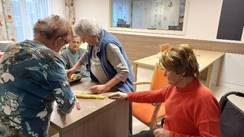 Ältere Frauen bereiten gemeinsam Teig an einem Tisch vor.