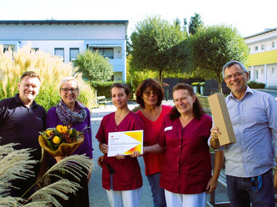 Gruppierung von Personen mit Zertifikat und Blumenstrauß im Freien.