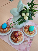 Osterdekoration mit Hasenfigur, gefärbten Eiern und Hefezöpfen auf einem Tisch.
