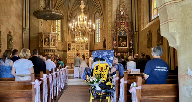 Eine festliche Zeremonie in einer Kirche mit Gästen und einem Rollstuhl im Vordergrund.