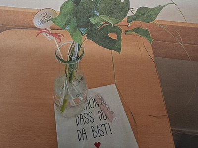 Ein roter Blumenstrauß in einer Glasvase steht neben einer Willkommenskarte.