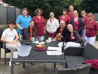 Gruppe von Personen in Arbeitskleidung versammelt im Freien um einen Tisch.