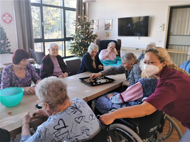 Ältere Menschen spielen gemeinsam mit Betreuungspersonal in einem gemütlichen Raum.