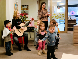 Kinder tanzen und klatschen, während eine Frau auf der Gitarre spielt.