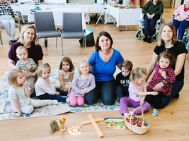 Eine Gruppe von Kindern und Erwachsenen sitzt auf einem Teppich mit Spielzeug.