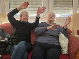 Zwei Frauen sitzen auf einem Sofa und gestikulieren fröhlich.