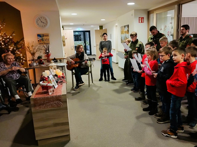 Kinder singen Weihnachtslieder, während eine Erwachsene Gitarre spielt.