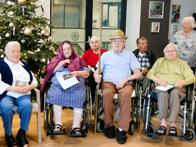 Sechs Senioren in Rollstühlen sitzen zusammen, umgeben von einem Weihnachtsbaum.