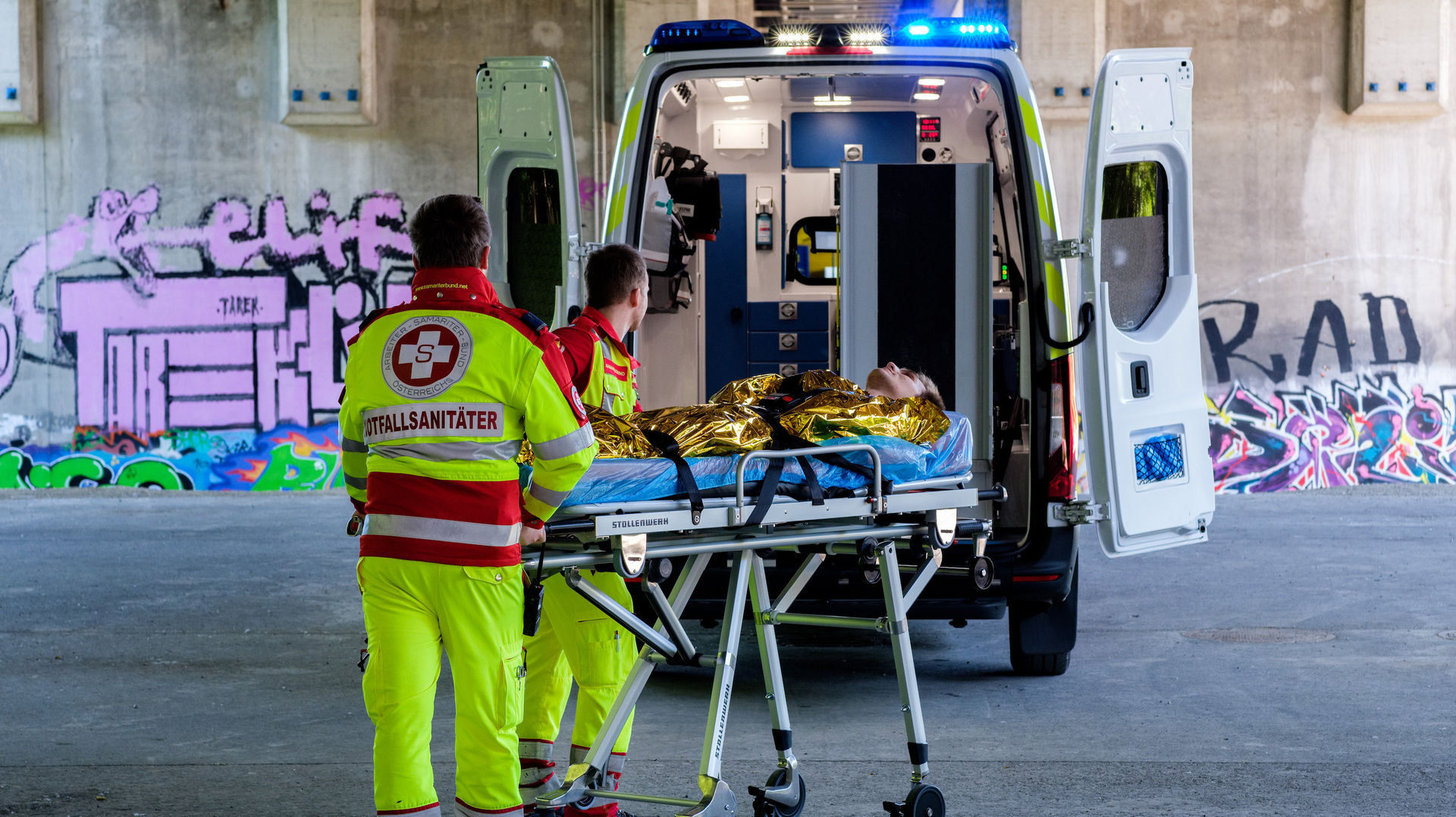 Zwei Samariterbund-Sanitäter mit Patienten auf der Krankentrage vor einem Rettungswagen