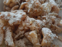 Frittierte Teigstücke, bestäubt mit Puderzucker, in einer weißen Schüssel.