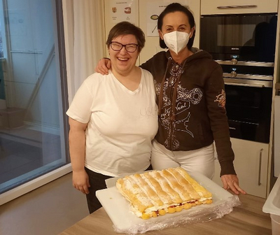 Zwei Frauen lächeln neben einem großen Kuchen auf einem Tisch.
