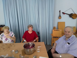Drei Senioren sitzen an einem Tisch mit Getränken und einem Topf.