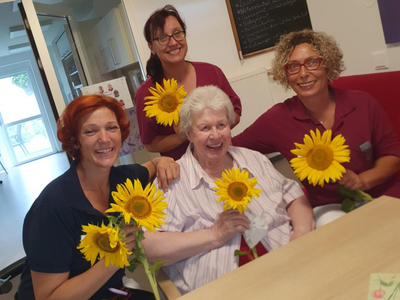 Vier Personen halten Sonnenblumen und lächeln fröhlich in einem Innenraum.