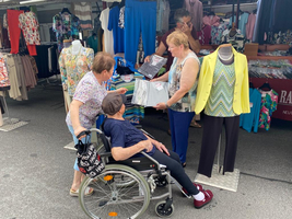 Vier Frauen, darunter eine im Rollstuhl, schauen sich Kleidung auf einem Markt an.