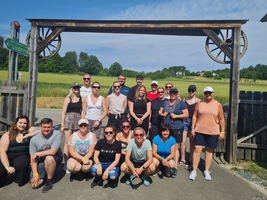 Gruppe von Menschen steht vor einem Holztor in der Natur.