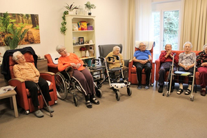 Eine Gruppe älterer Menschen sitzt in einem Gemeinschaftsraum.